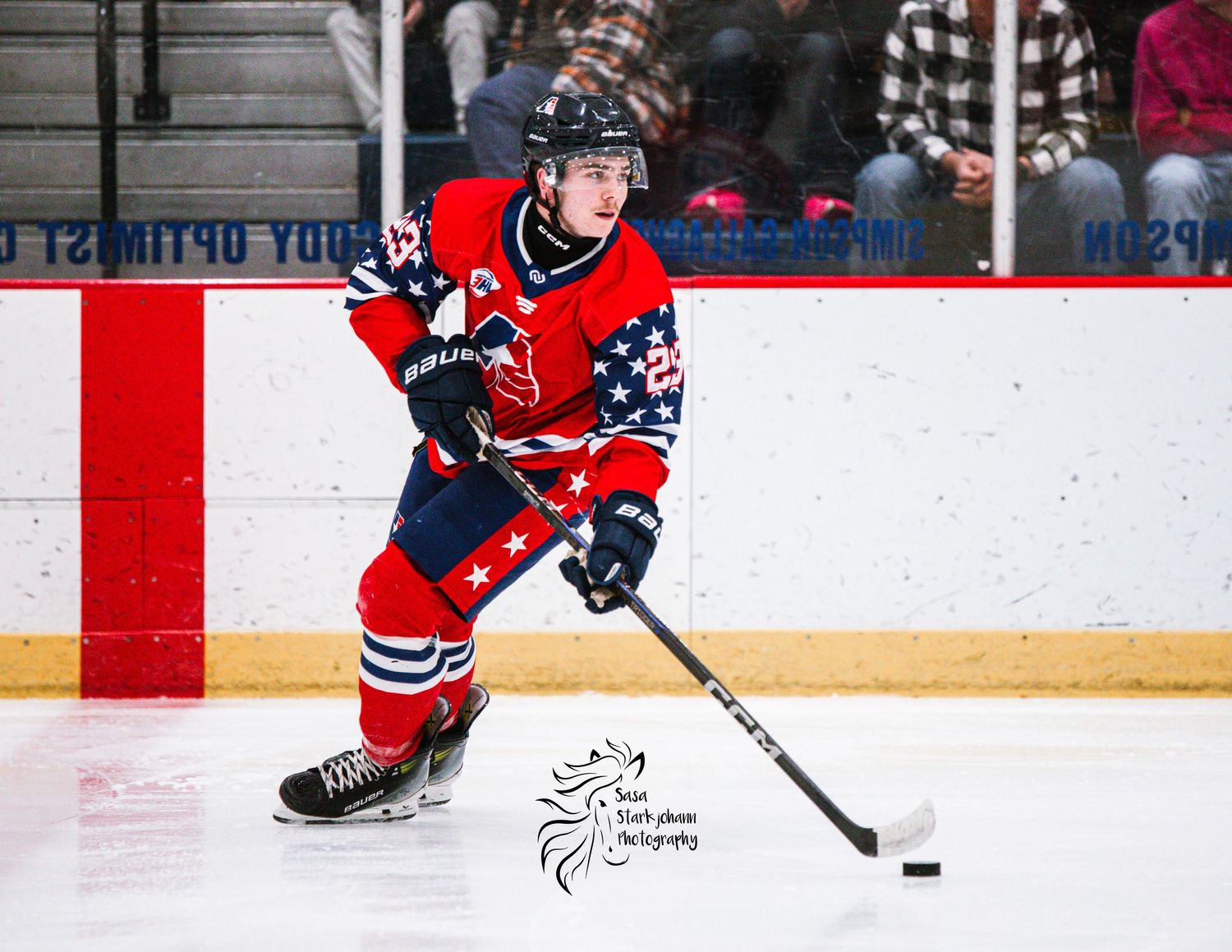 Hockey player in red jersey skating with puck during competitive match.