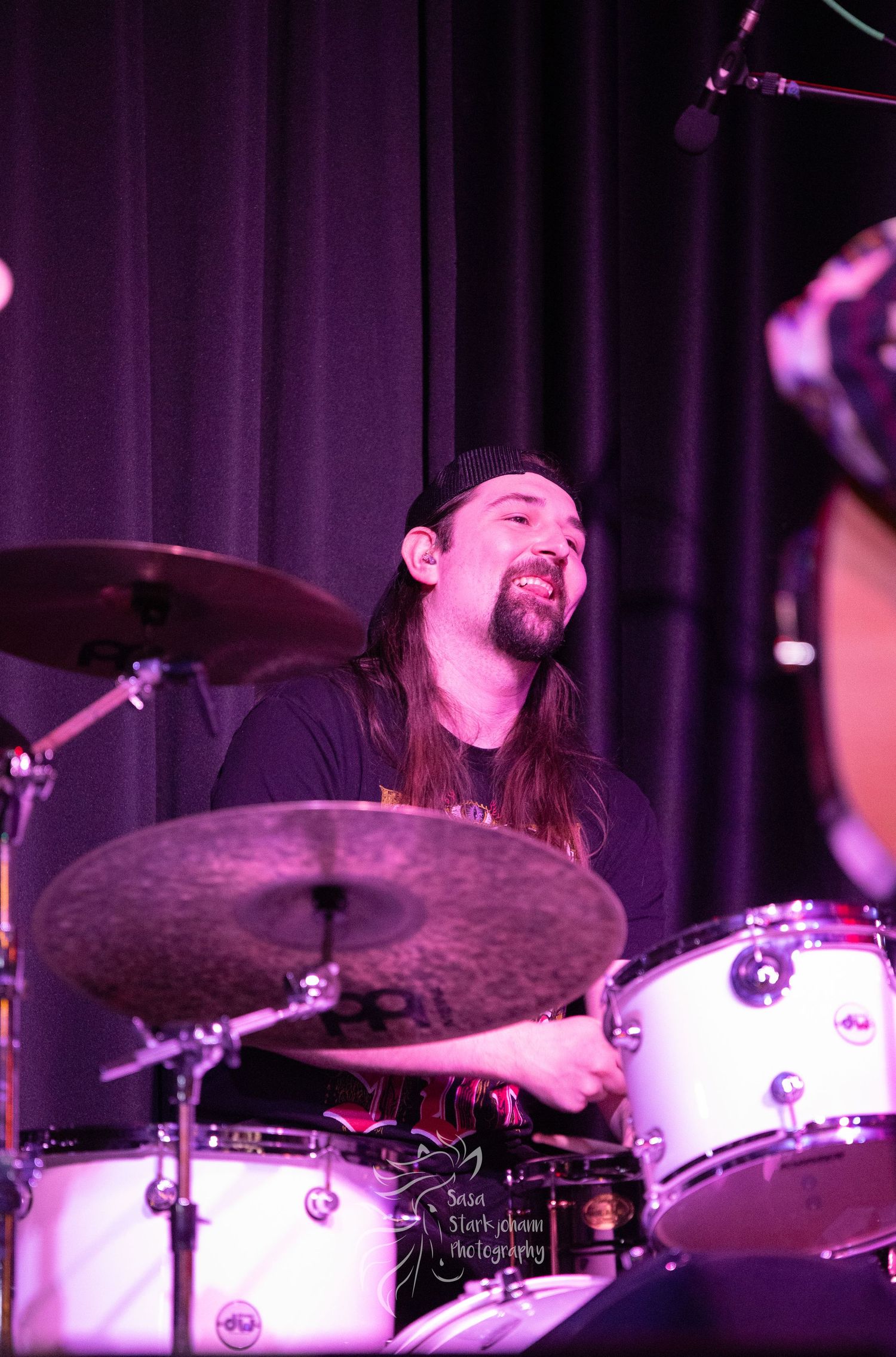Drummer performing enthusiastically behind a white drum kit on stage.
