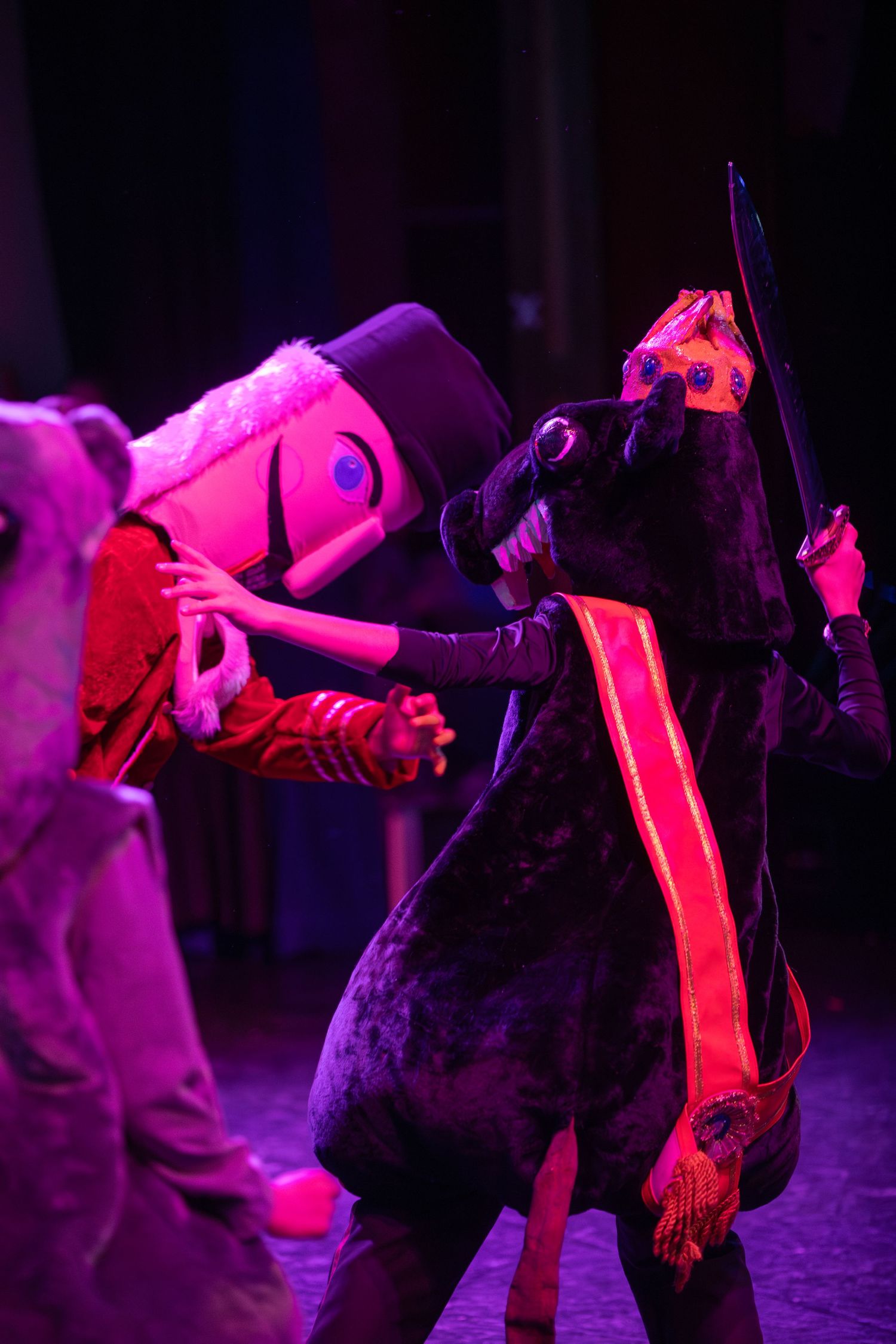 Ballet dancer in silhouette performing with another figure under dramatic red and purple lighting.