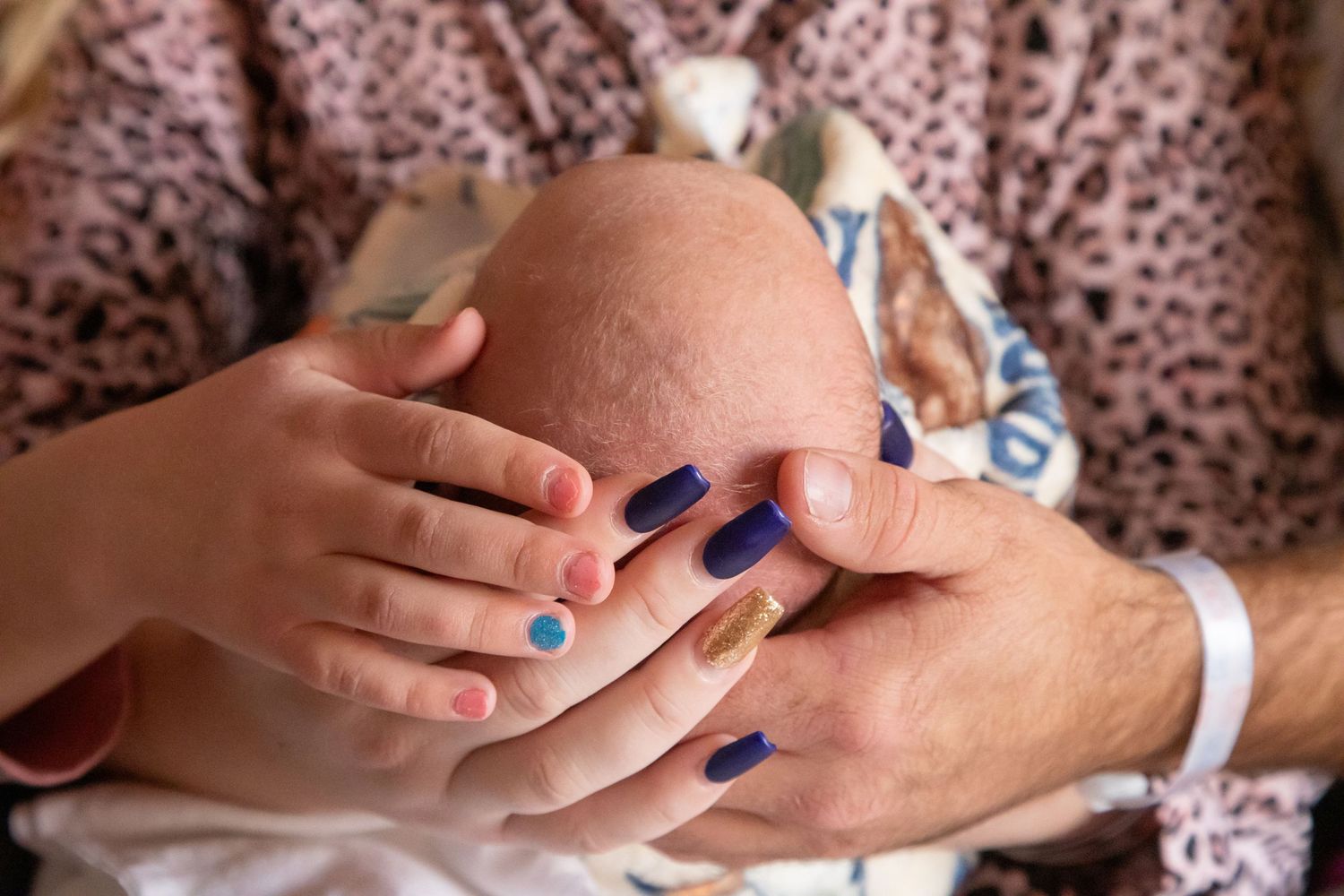 Close-up of hands with blue nail polish gently cradling a newborn baby's head.