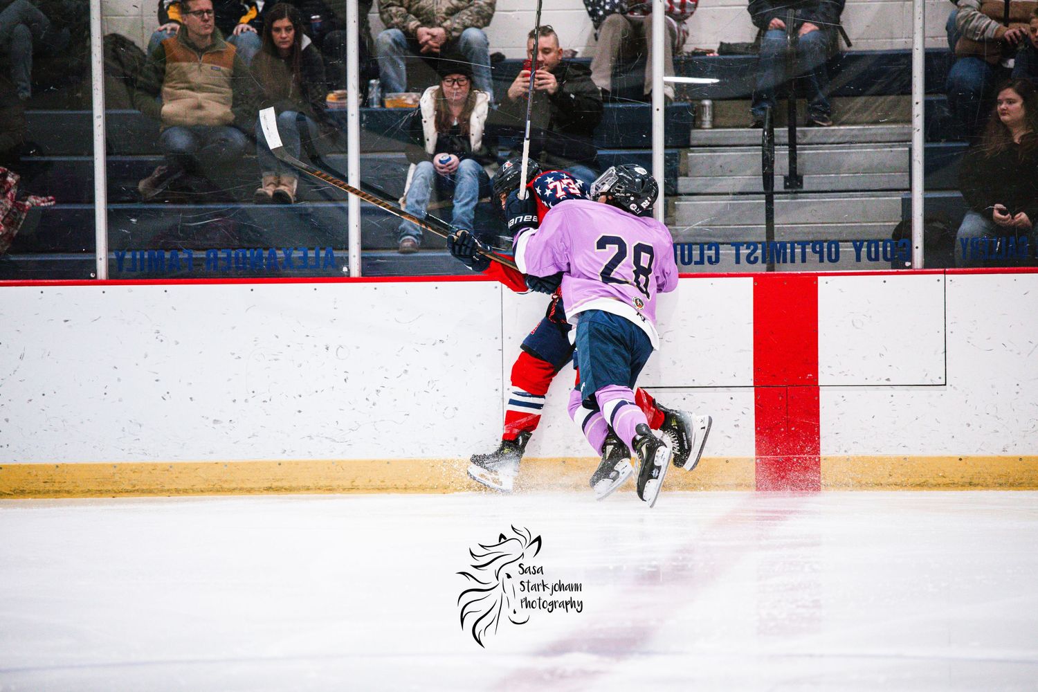 Player in pink jersey checks opponent into boards during intense hockey game.