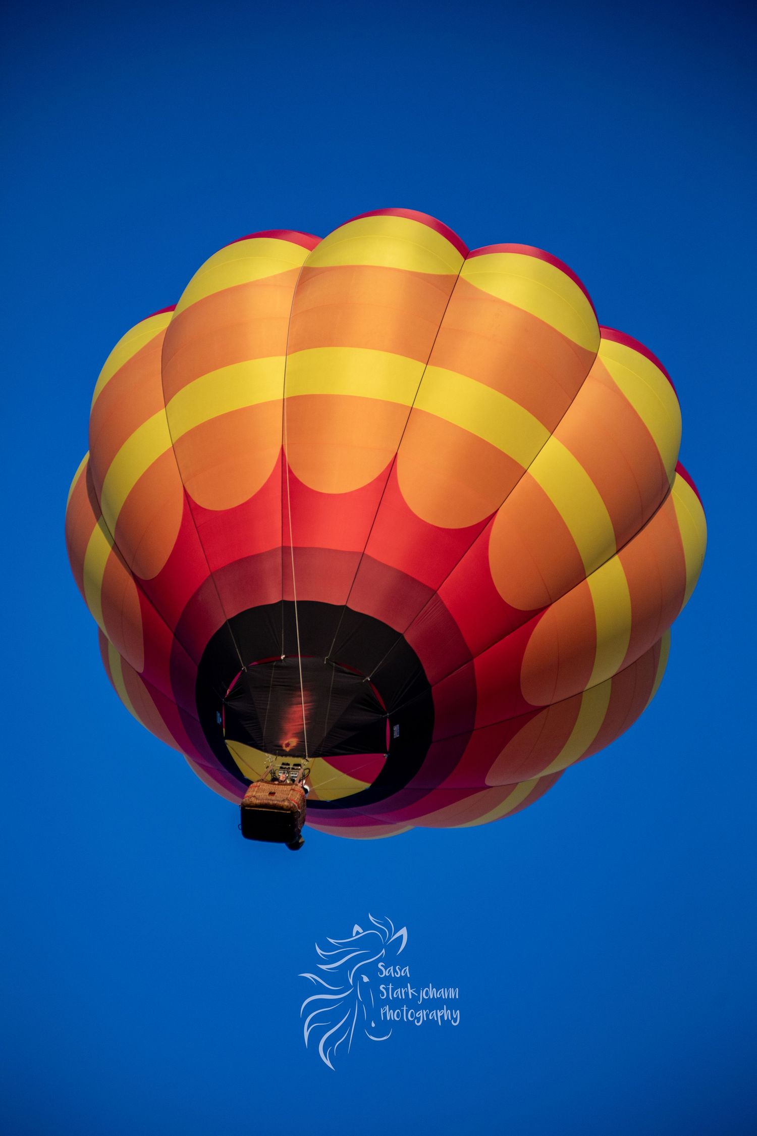Hot air balloon silhouetted against deep blue sky shows sequential motion as it deflates and descends at sunset.