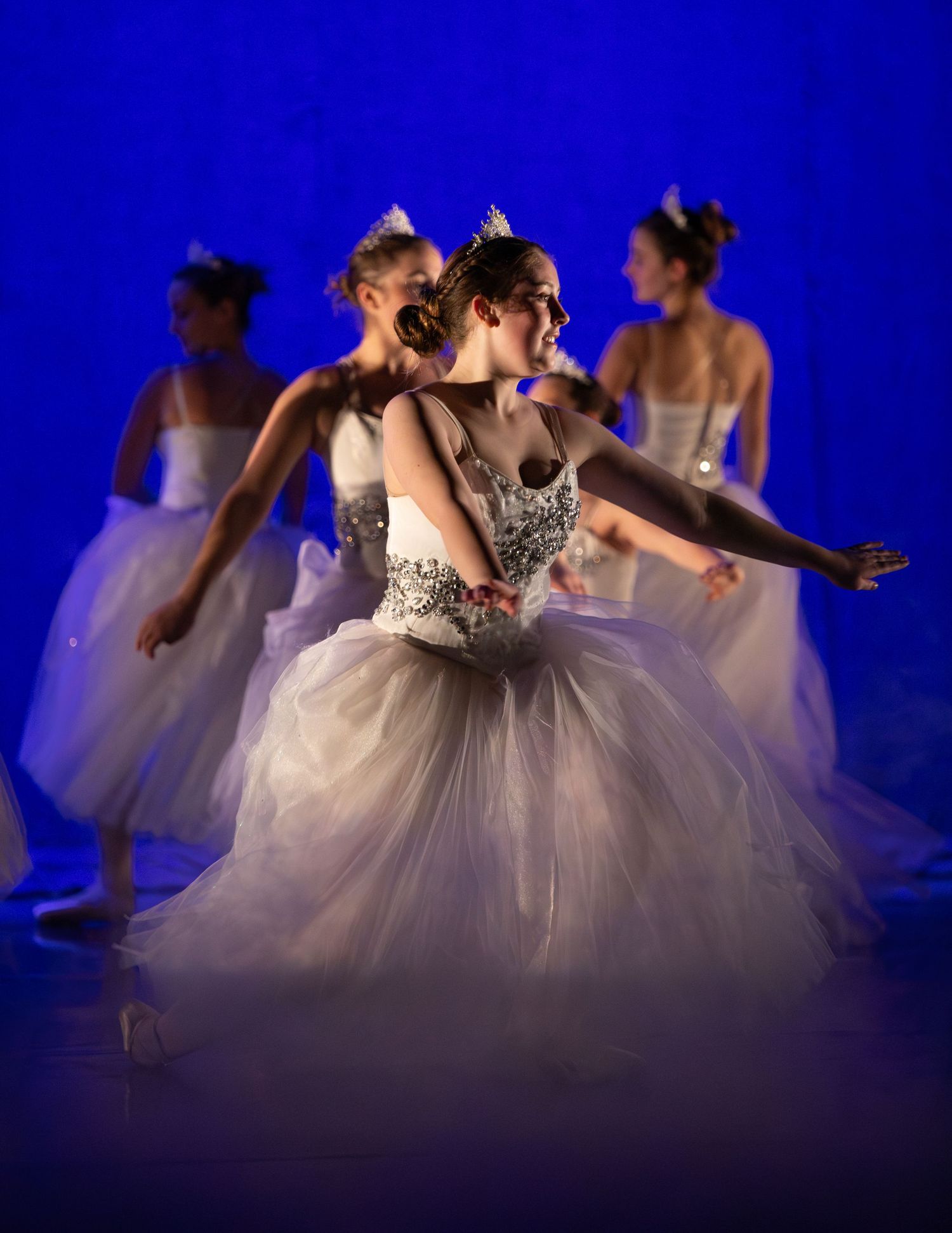 Ballet dancers in white tutus perform ensemble dance against blue background.