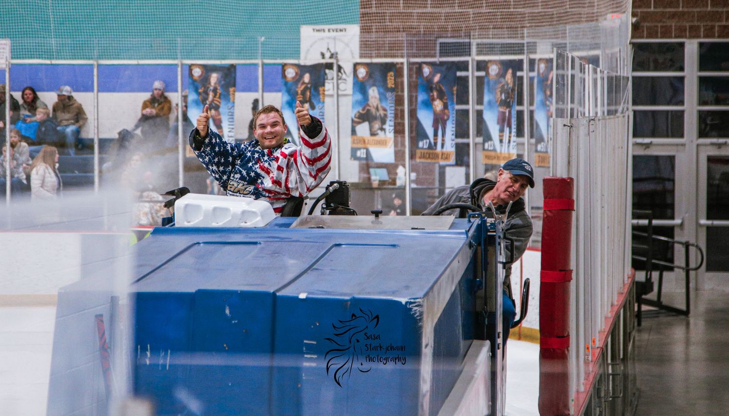 Spectators watch a game from behind protective glass barriers at an indoor sports venue.