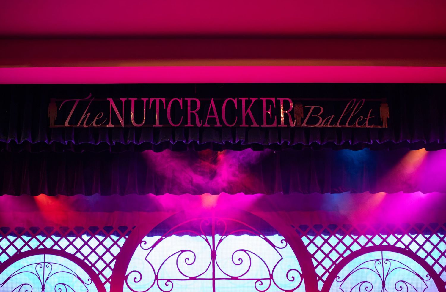 Illuminated Nutcracker Ballet stage set with ornate ironwork and dramatic purple lighting.