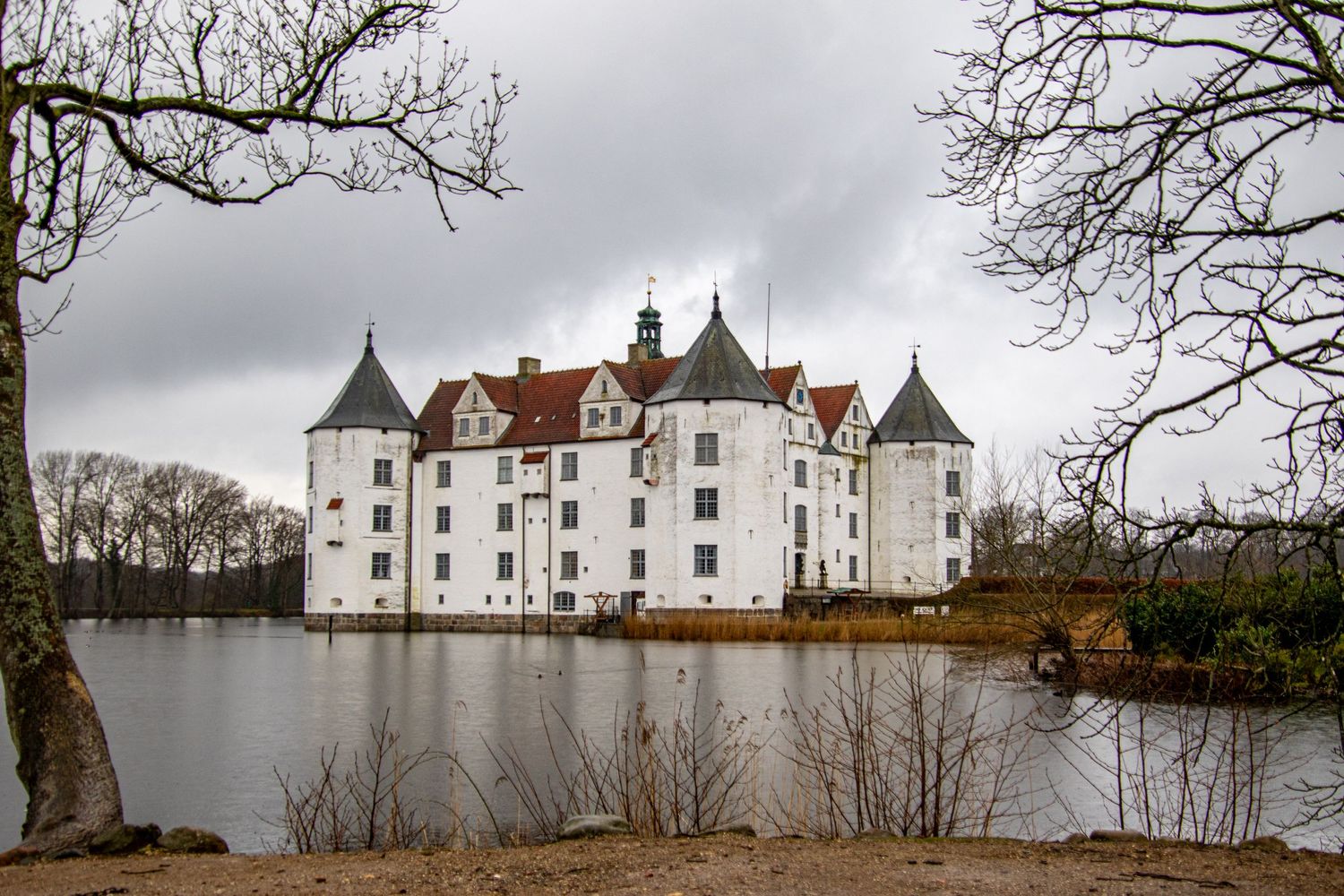 White castle-like structure with multiple towers reflects in surrounding moat under cloudy sky.