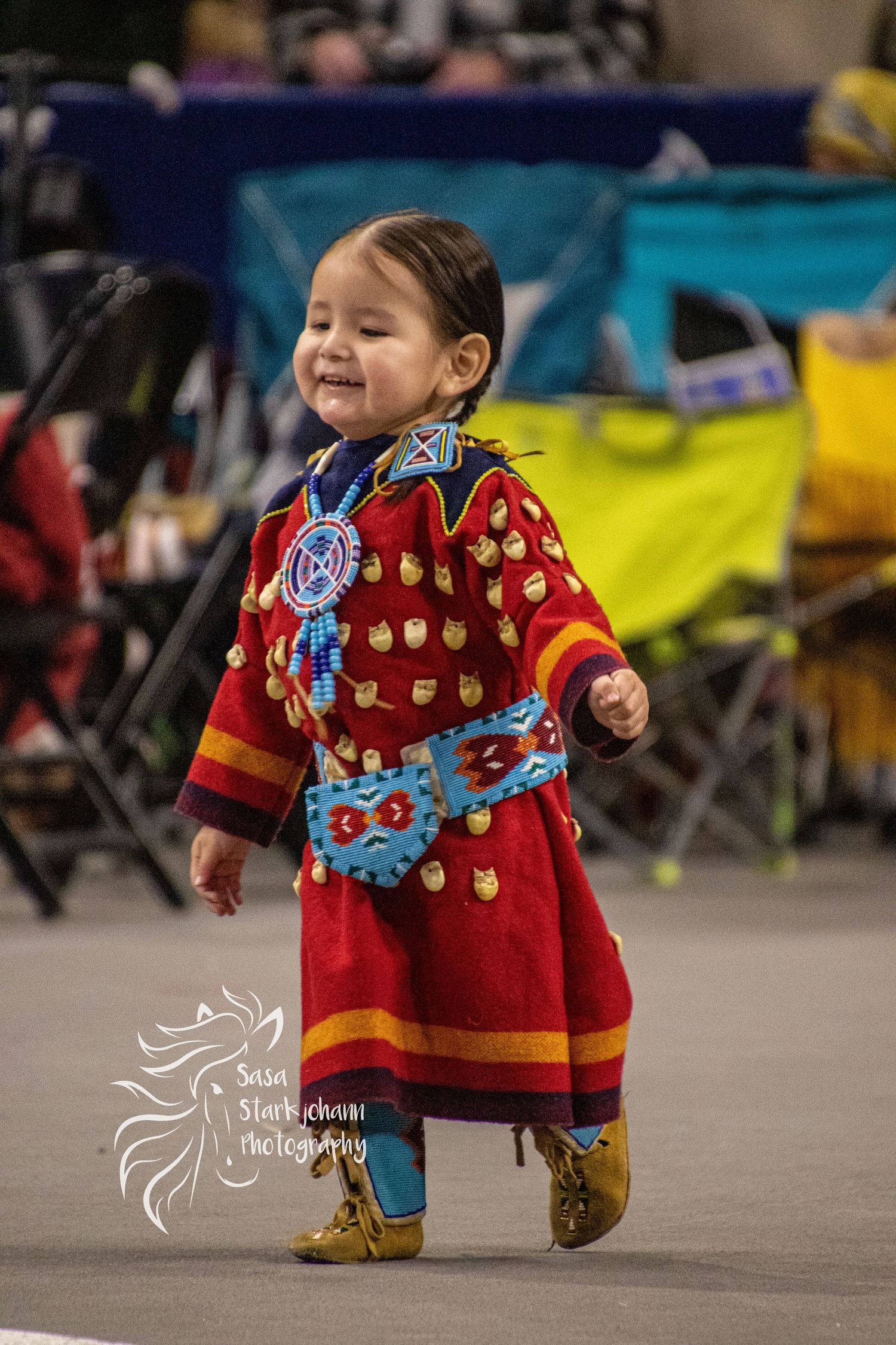 Young dancer in traditional red and blue beaded regalia at Native American powwow celebration.