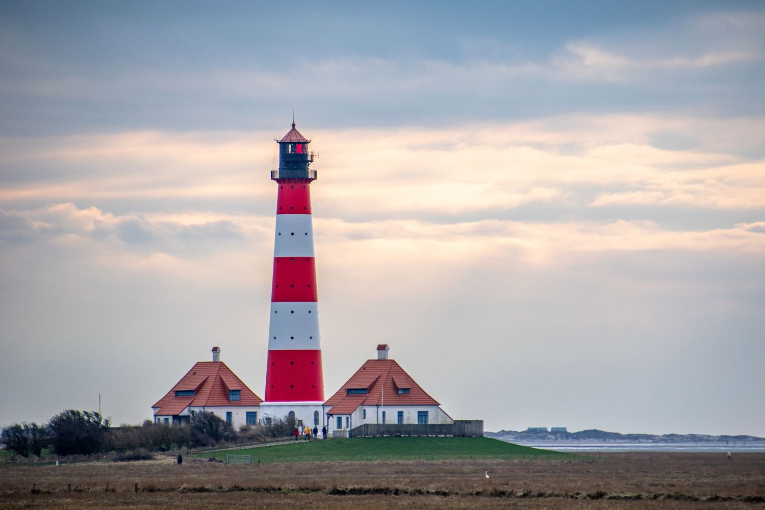 Red and white striped lighthouse stands tall against cloudy coastal sky at sunset.