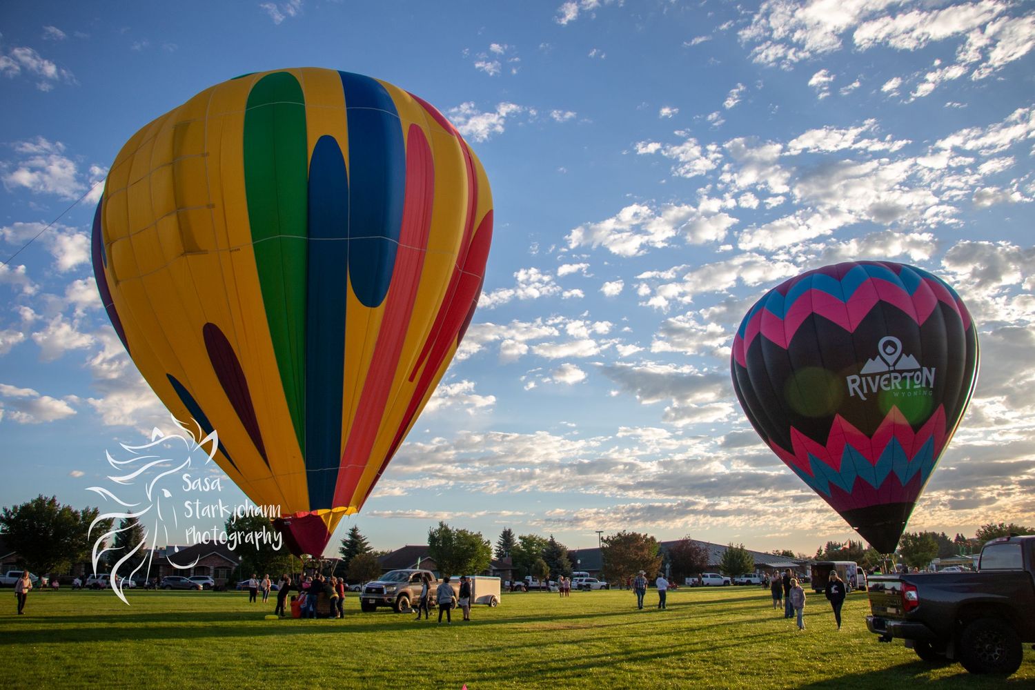 Colorful hot air balloons preparing for launch in a grassy field at sunset.