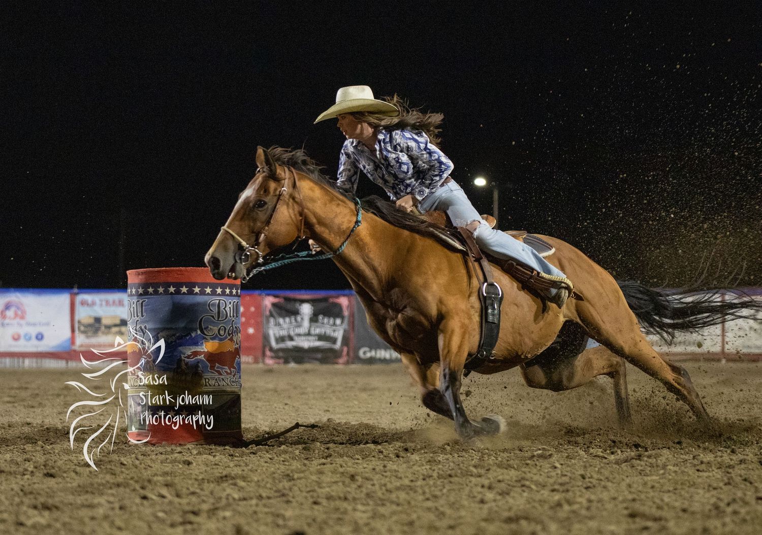 A barrel racer on horseback competes at a nighttime rodeo event.