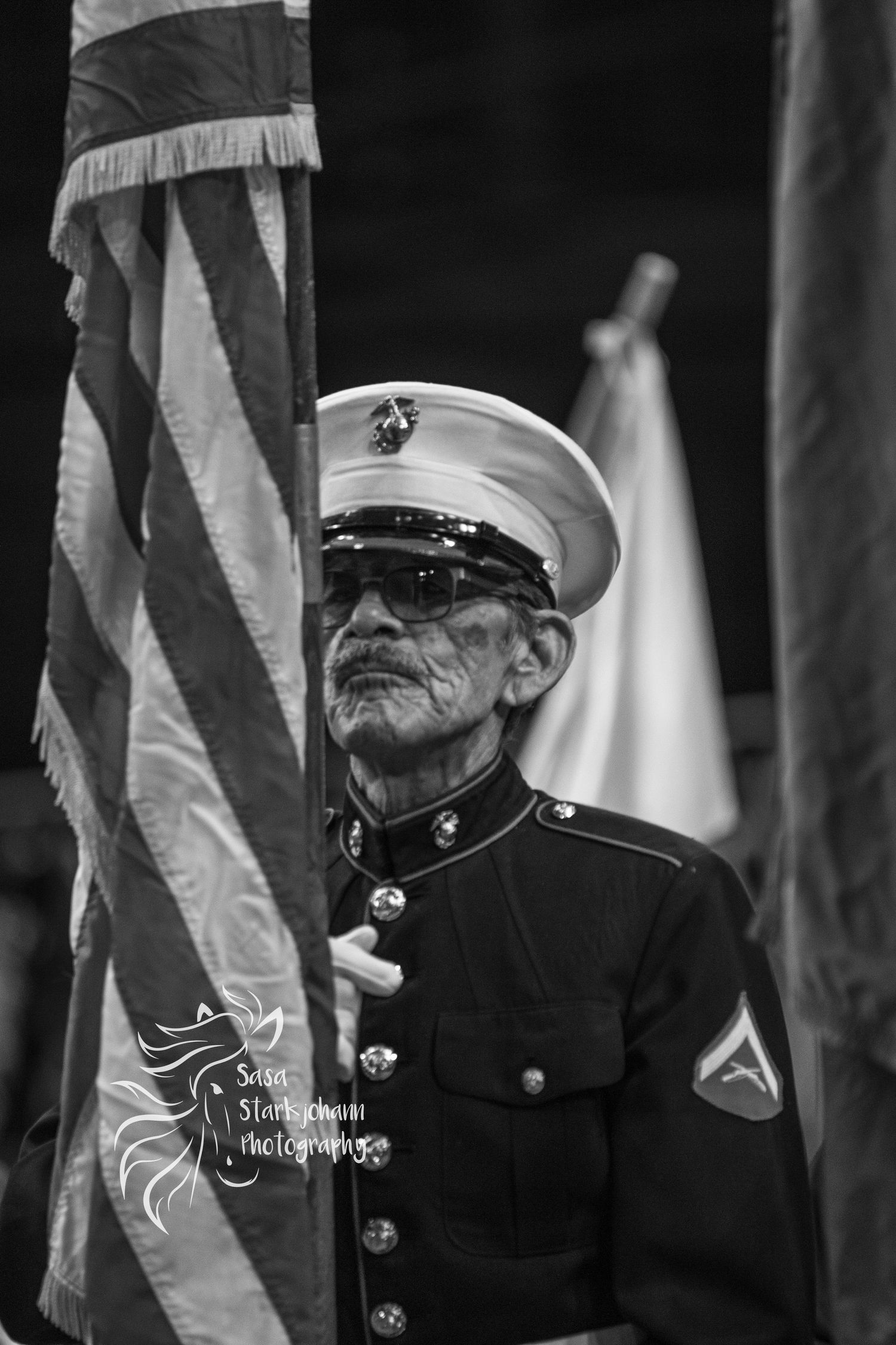 Marine Corps veteran in dress uniform standing at attention next to American flag.