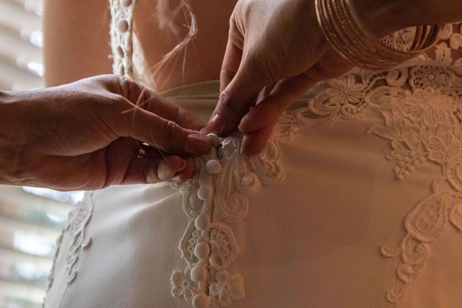 Close-up of hands buttoning delicate lace details on a wedding dress.