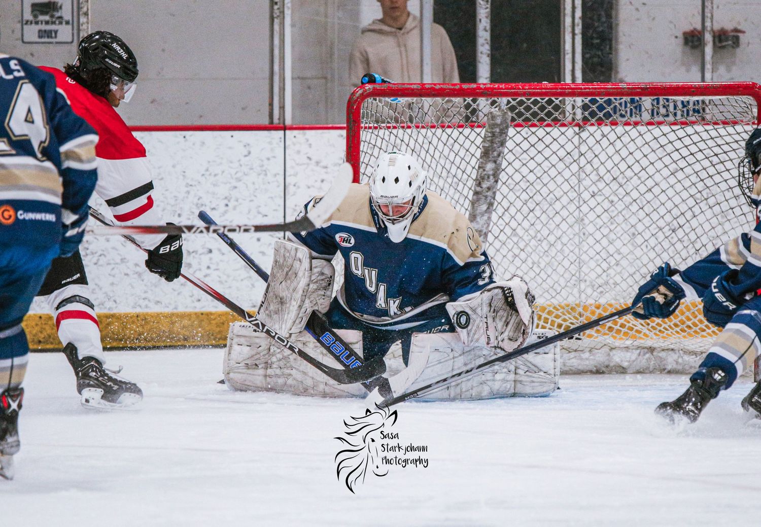 A dramatic save attempt by a hockey goalie as players converge on the net.