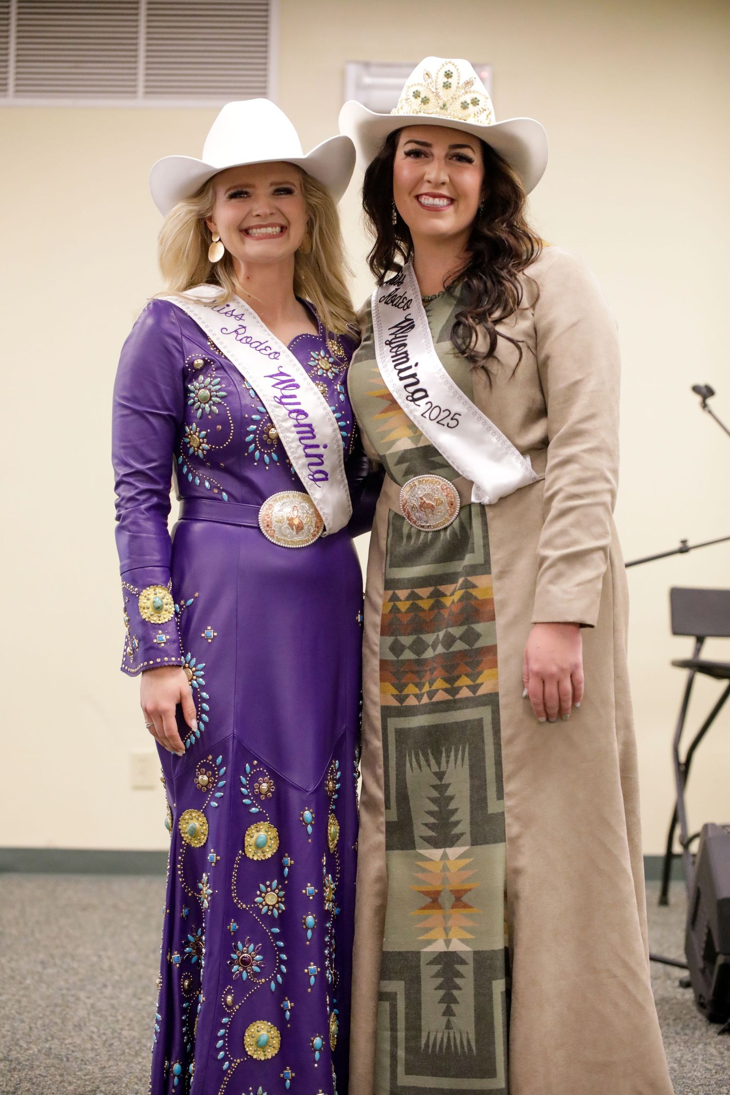 Two pageant winners in western attire and crowns posing together at indoor event.
