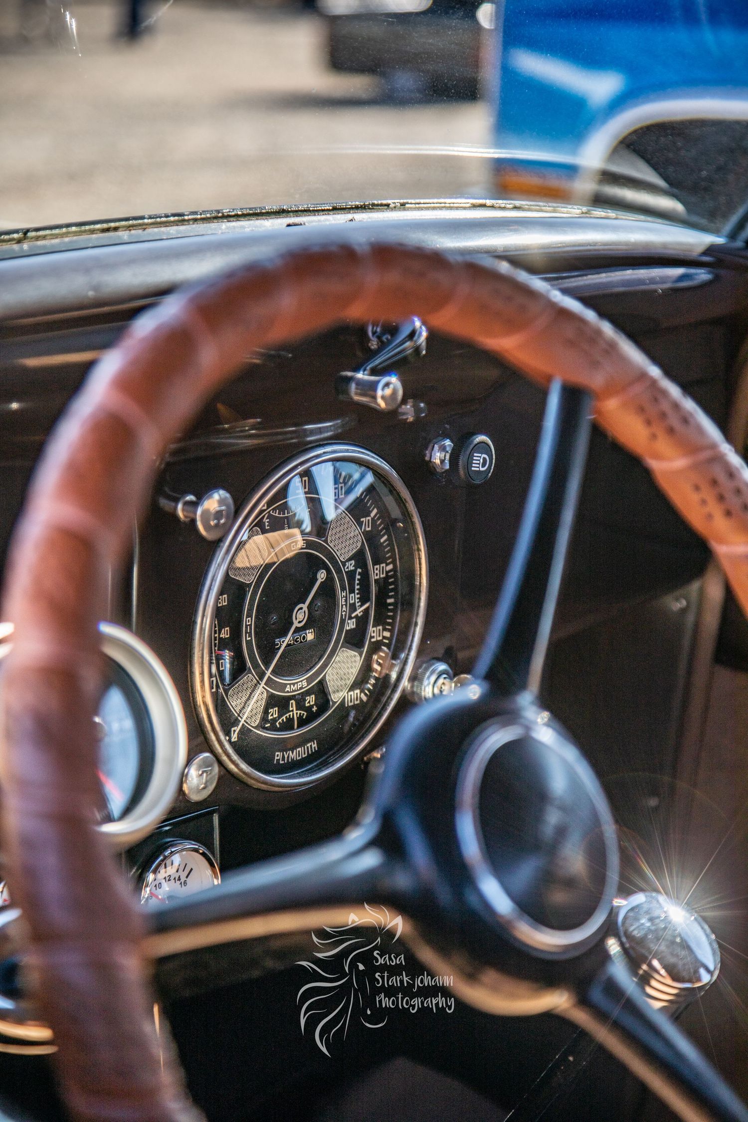 Vintage car dashboard with wooden steering wheel and classic round speedometer gauge against black interior.