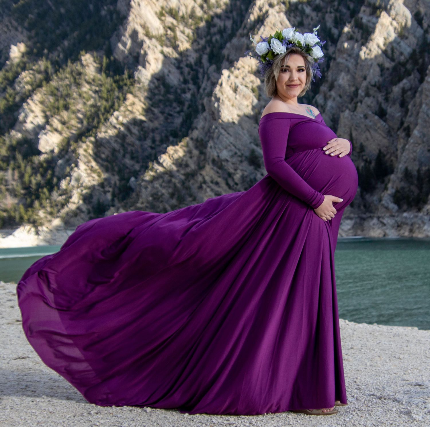 A maternity photo featuring a flowing purple dress against a dramatic mountain lake backdrop.