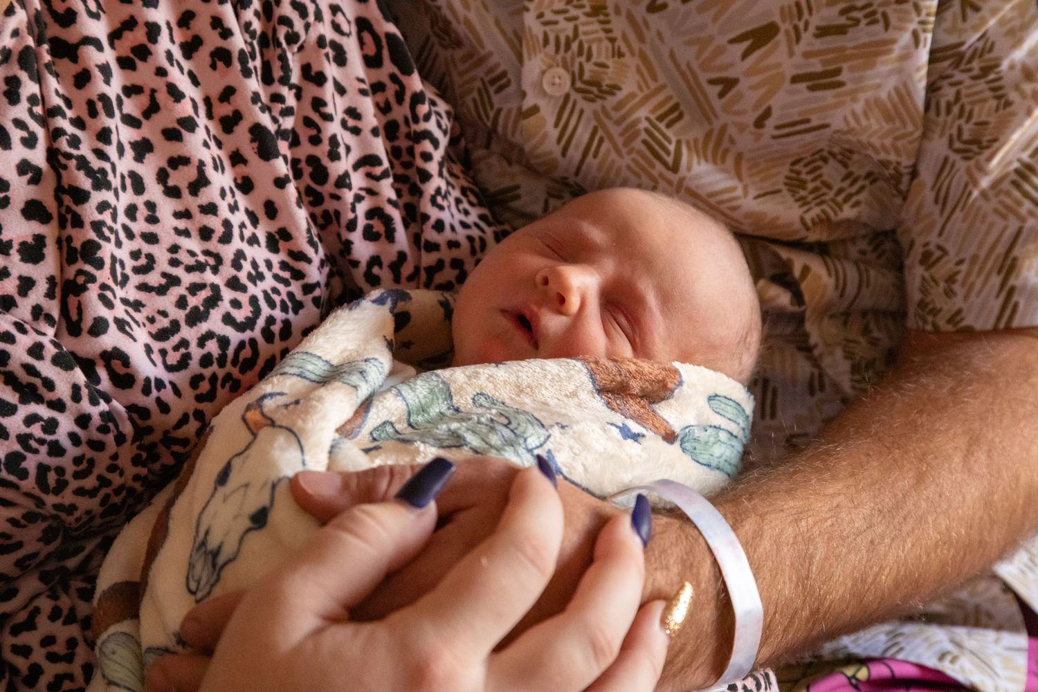 A newborn baby sleeps peacefully wrapped in a patterned blanket.