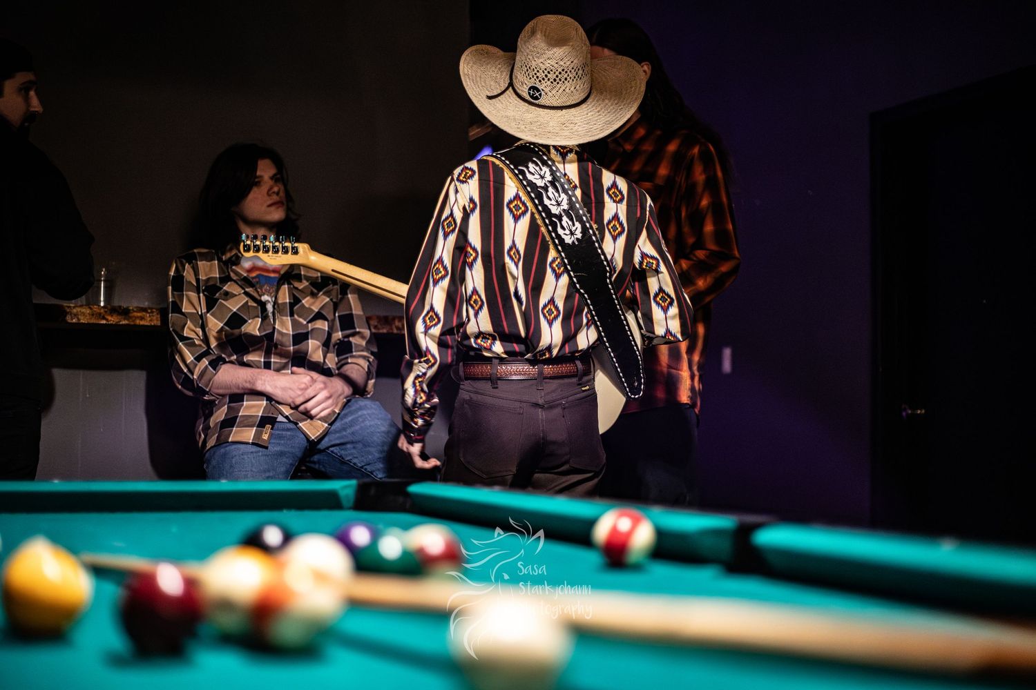 Person in western attire by pool table in dimly lit room.
