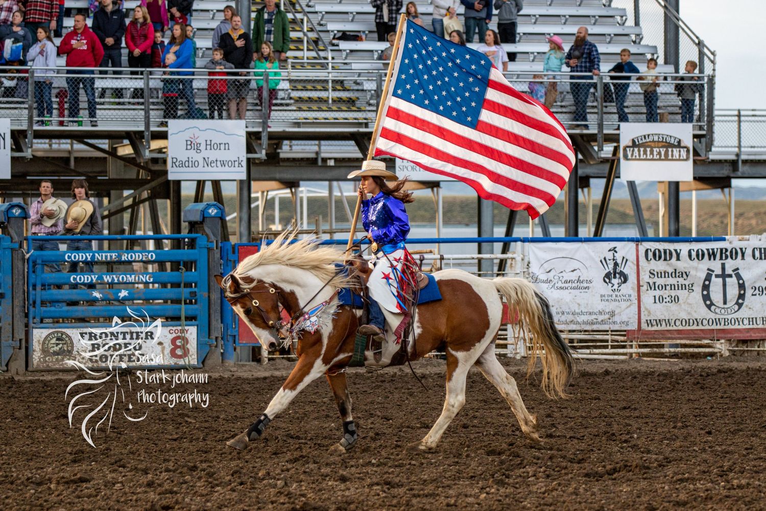 Rider carries American flag on horseback during rodeo performance.
