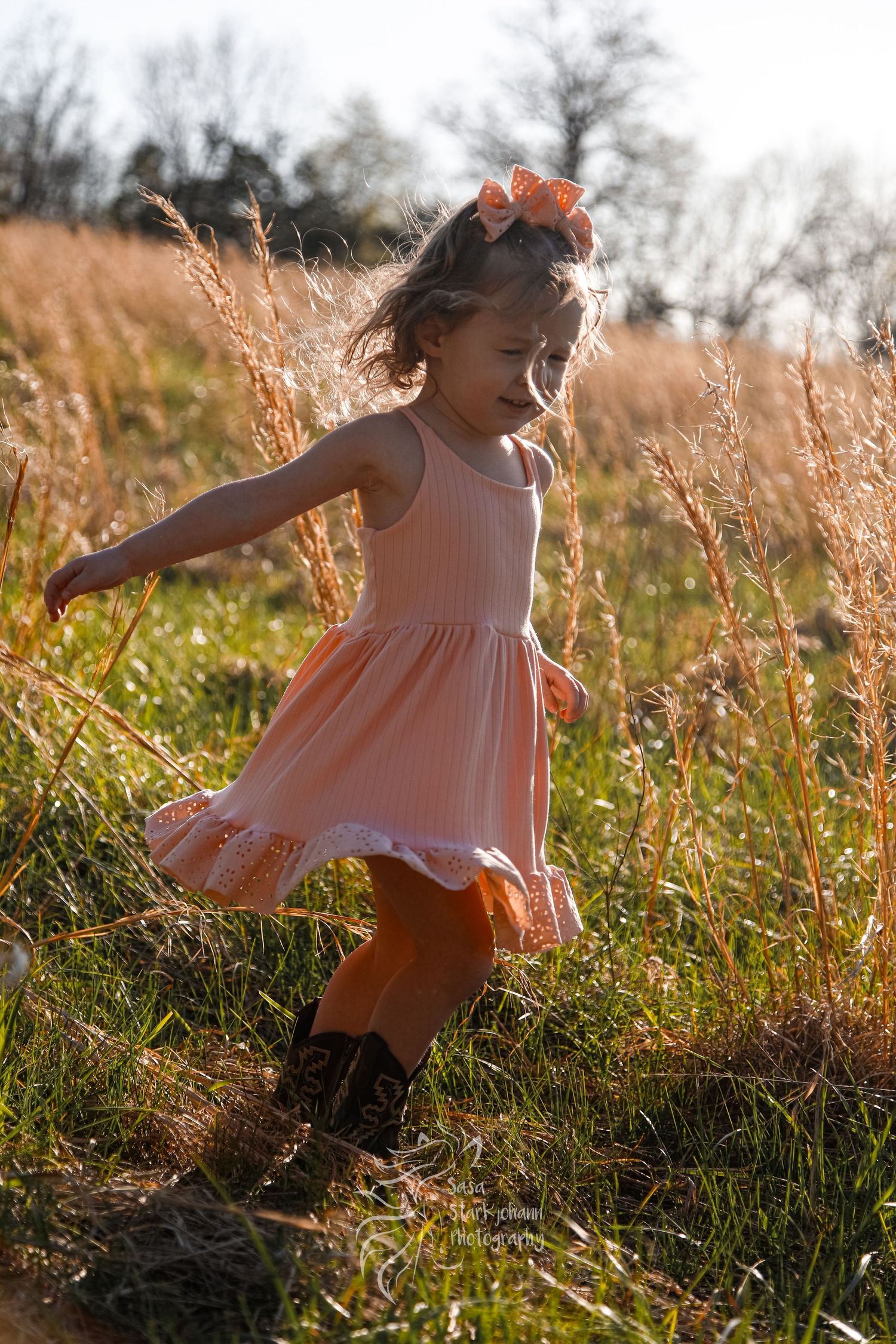 A young dancer twirls in a pink dress among tall grass at sunset.