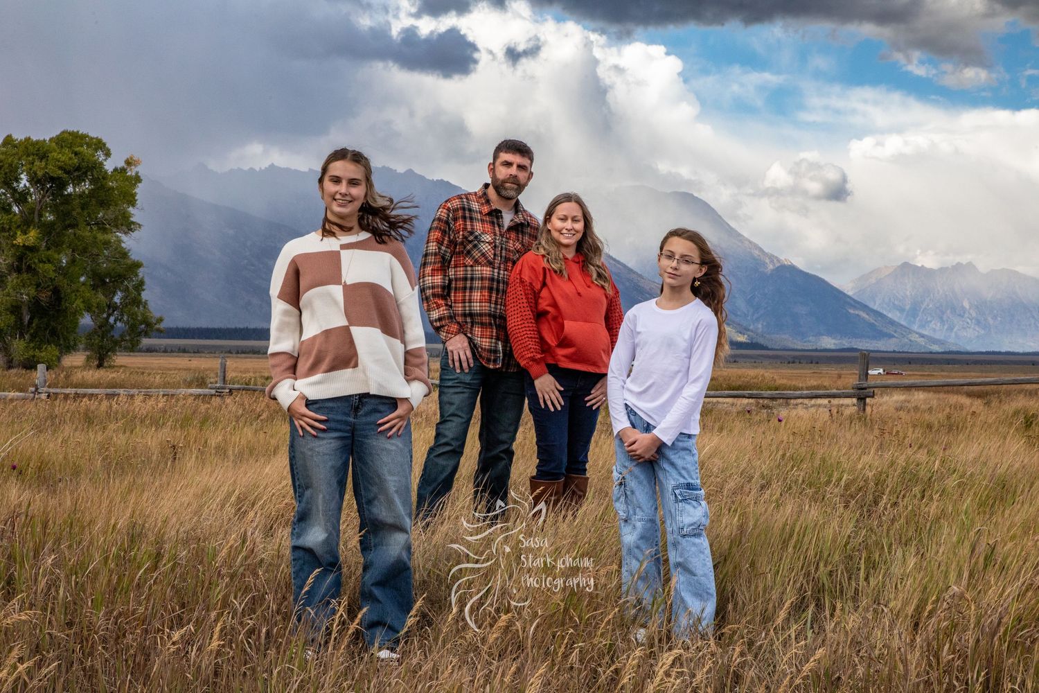Group sitting together in a grassy field with mountain landscape and dramatic clouds in the background.