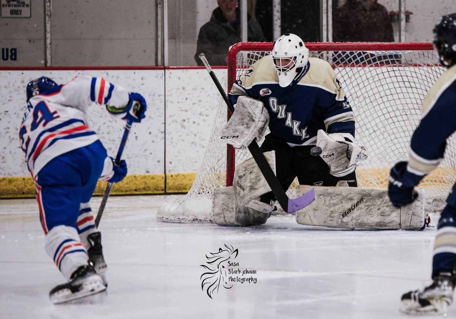 A hockey goalie defends the net as an opposing player attempts to score.