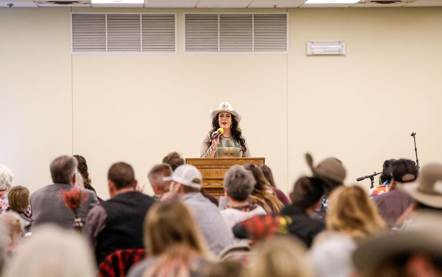 Speaker addressing audience from wooden podium during indoor gathering.