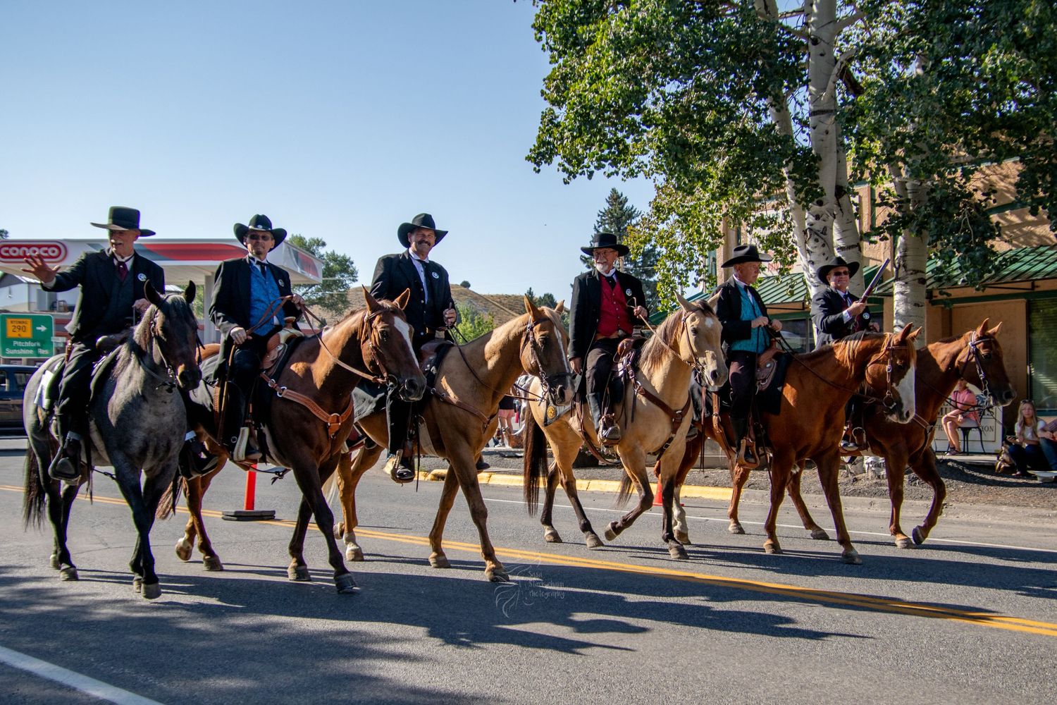 Horse riders in traditional western clothing parading down a tree-lined street.