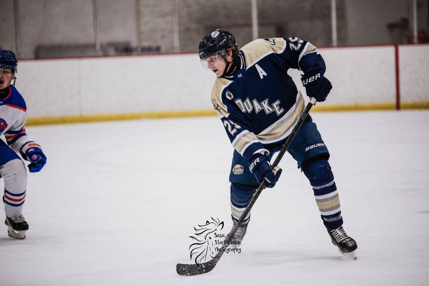 Hockey player in navy and tan jersey carries puck across ice during game action.