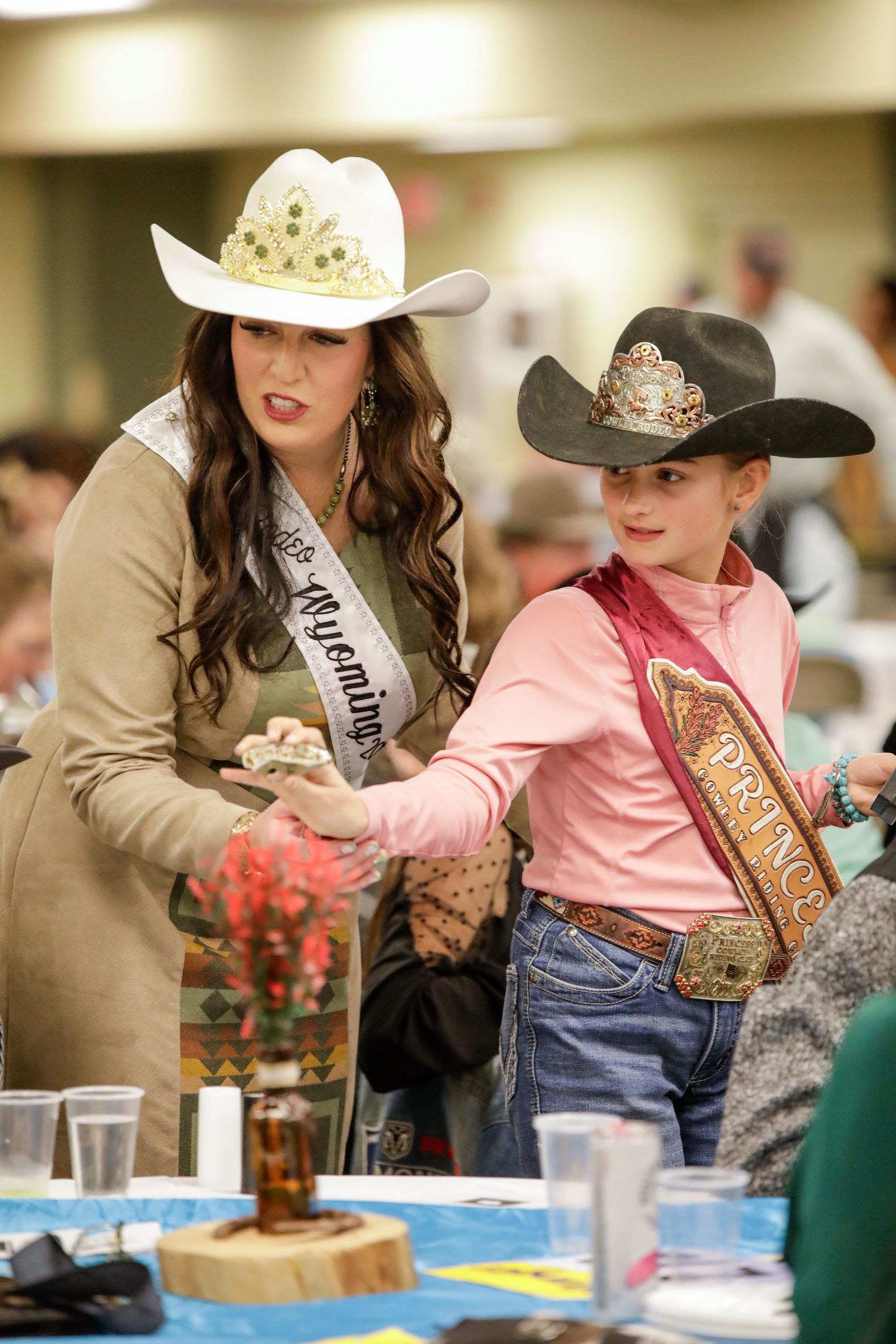Pageant contestants in cowboy hats serving food at western-themed event.