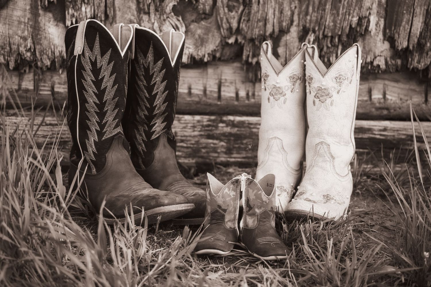 Black and white image of two pairs of cowboy boots positioned in tall grass.