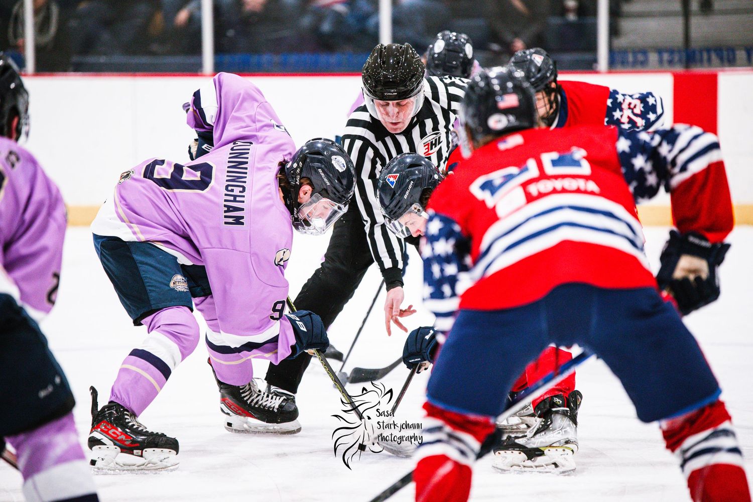 A face-off between teams in purple and red jerseys with referees overseeing the hockey game.