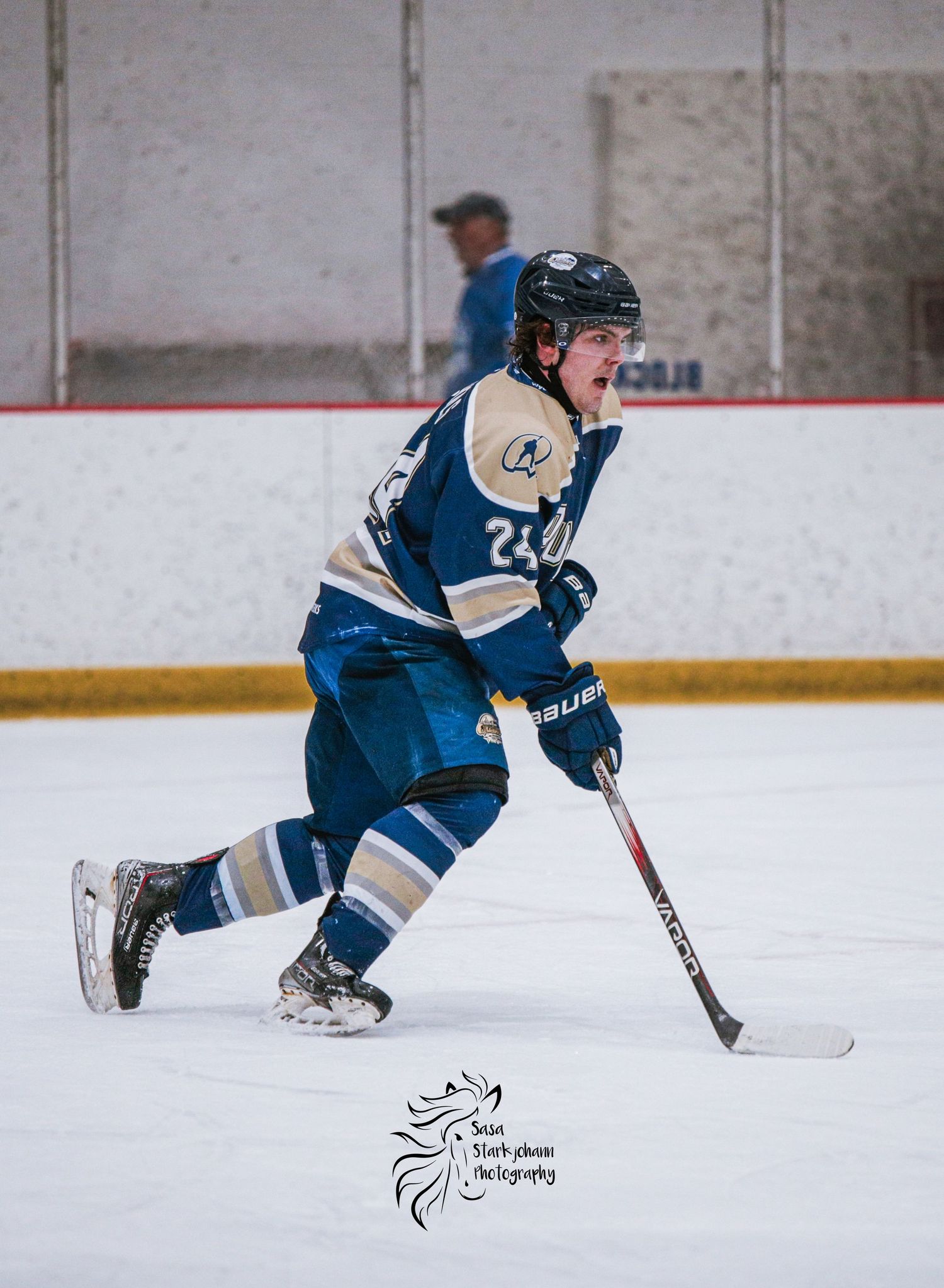 Ice hockey player in blue jersey skating with stick during game.