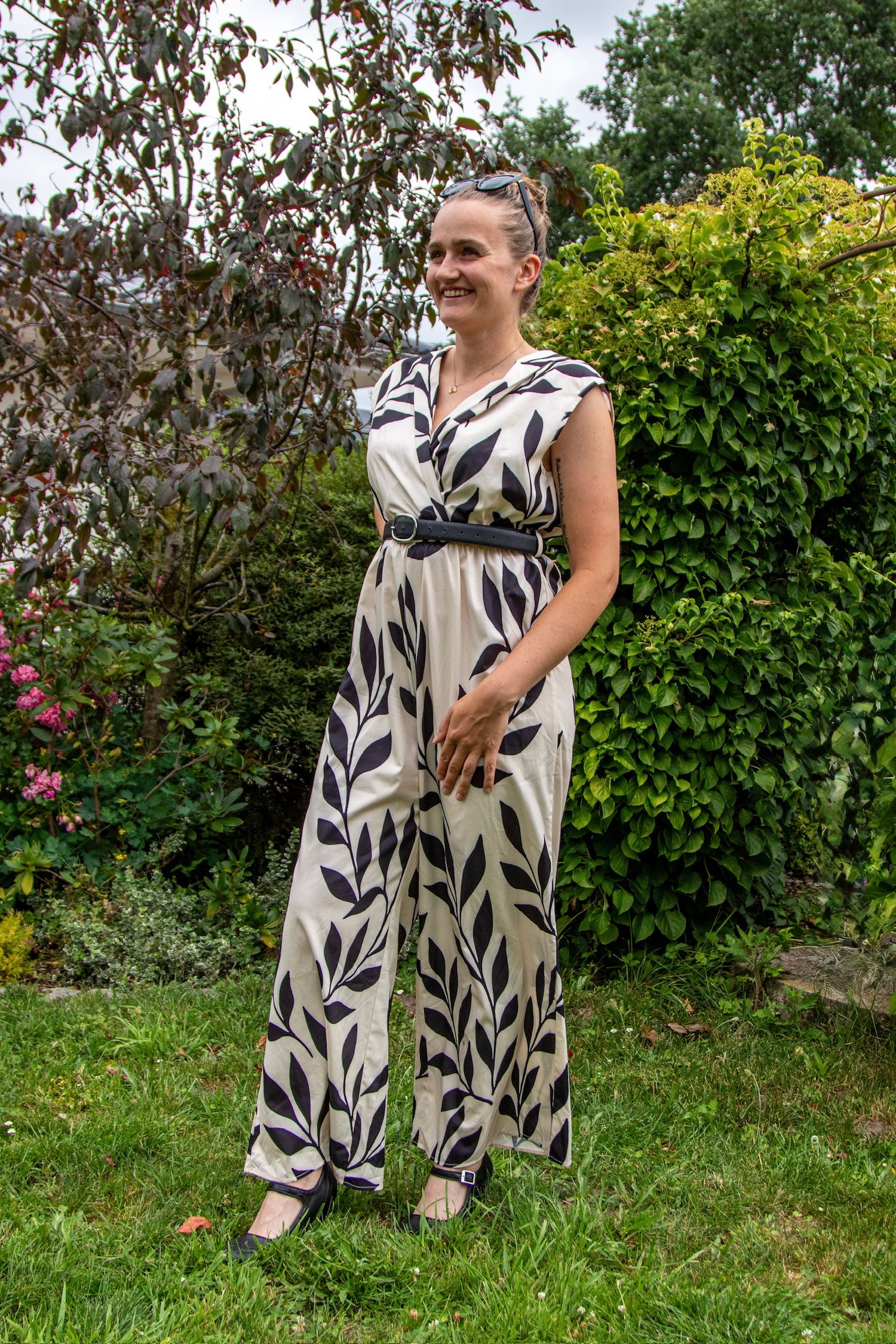 Woman in floral leaf-print jumpsuit smiling outdoors in a lush green garden.