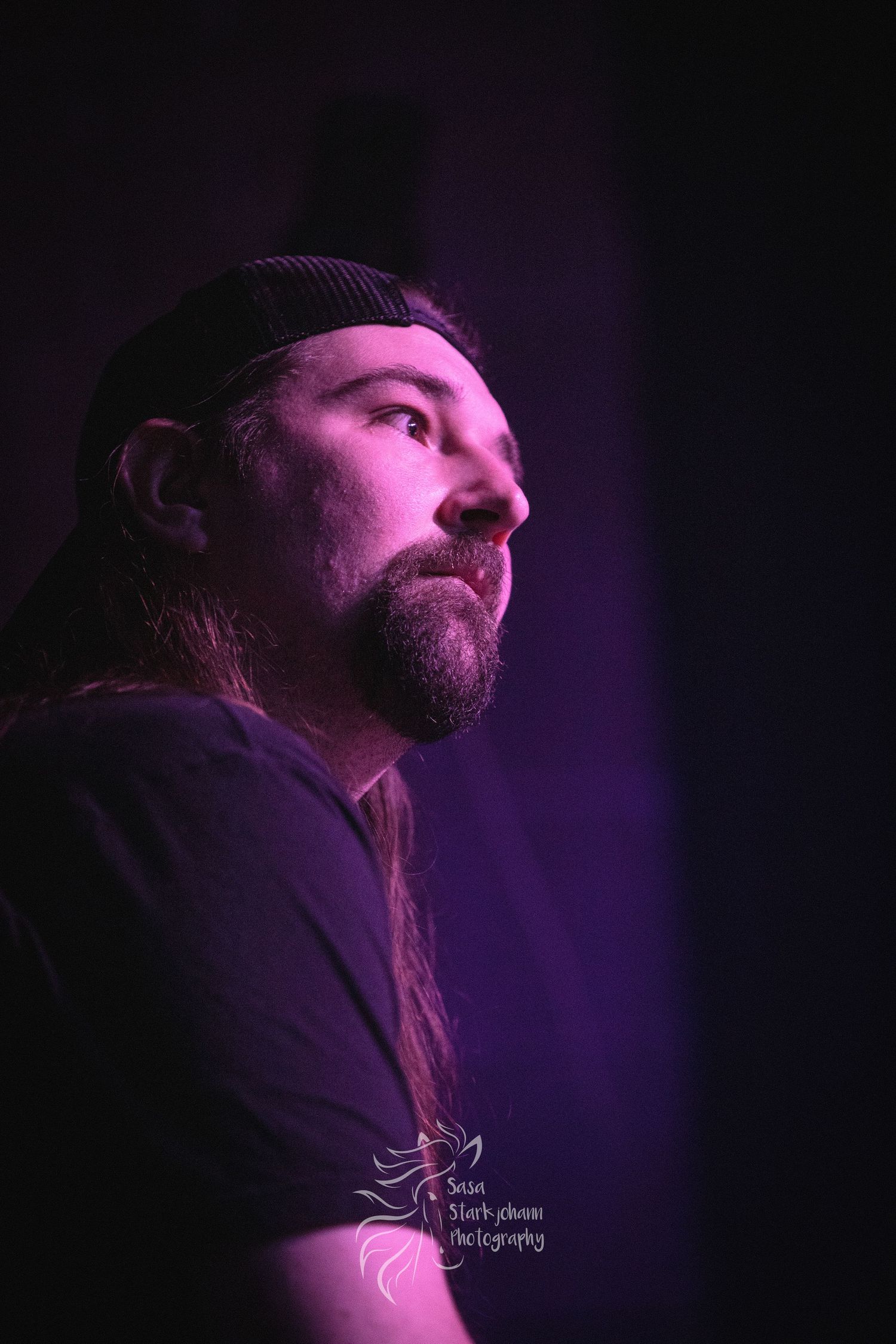 An artistic side profile portrait lit by purple stage lights against a dark background.
