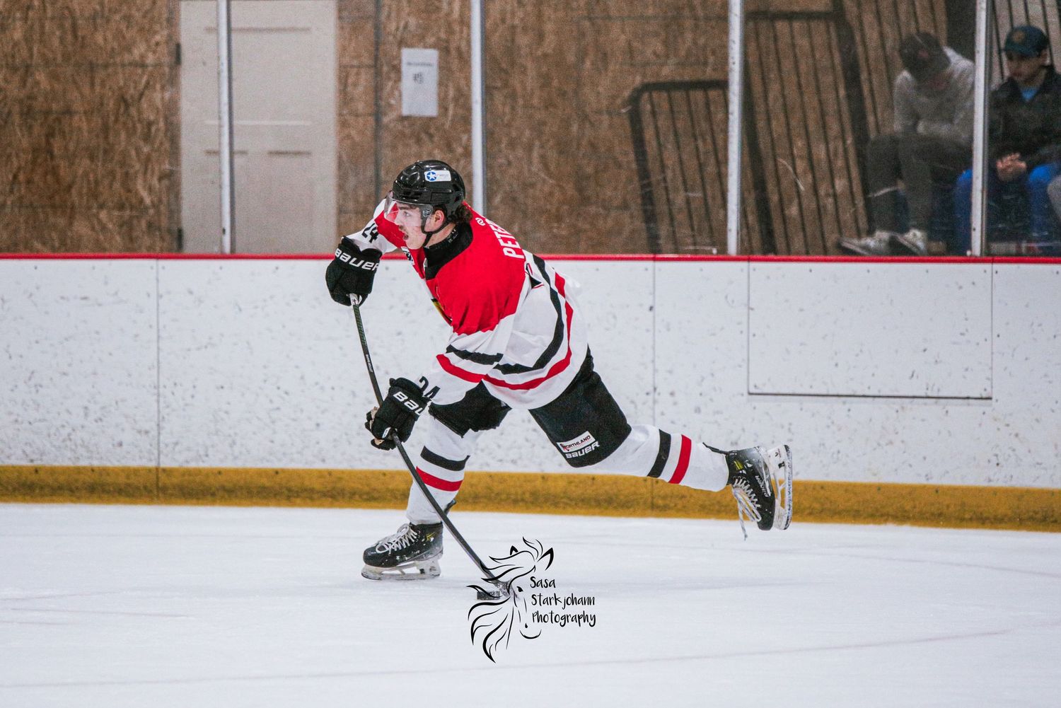 Hockey player in red and white jersey takes dynamic shooting stance on ice.