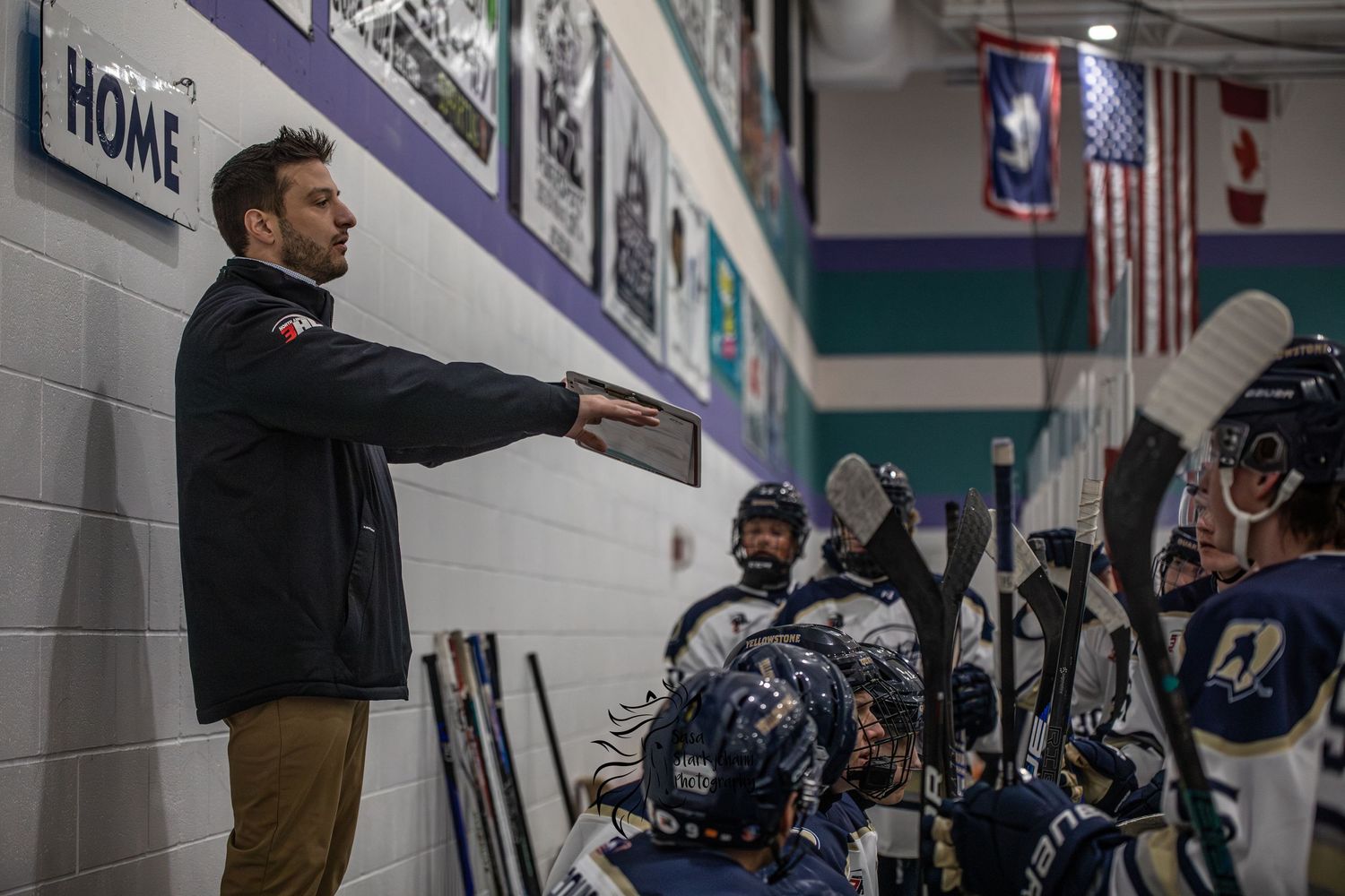 Hockey coach giving instructions to players in gear near rink boards during a team huddle.