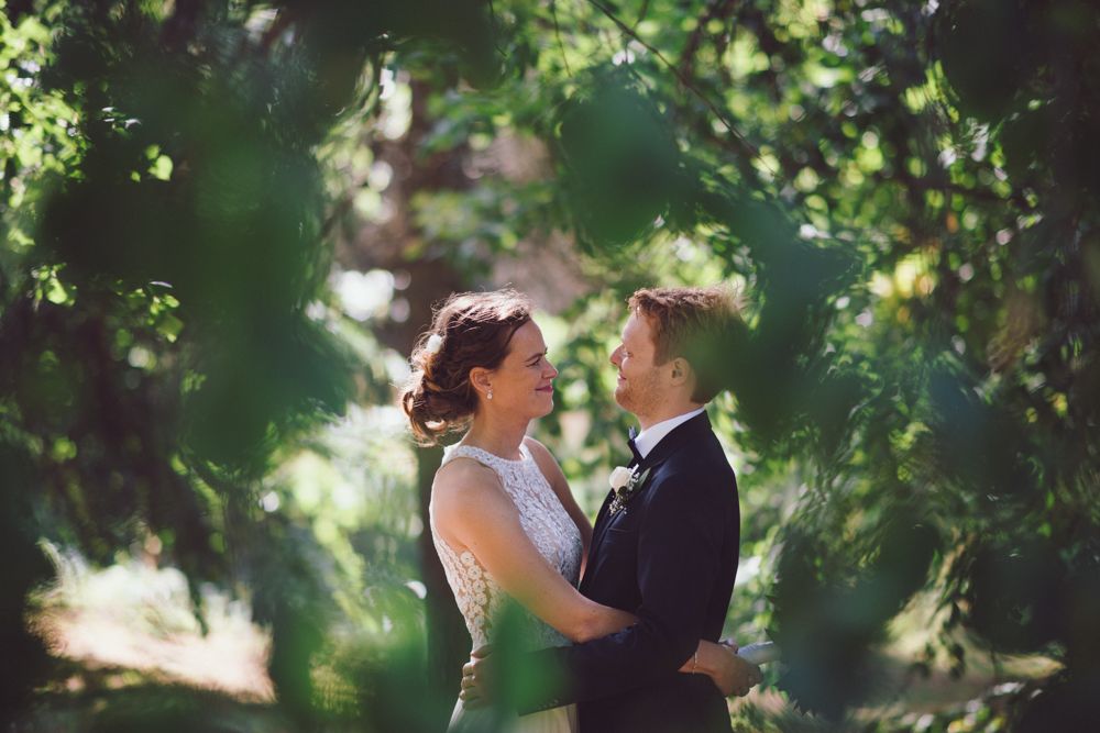 An intimate wedding moment captured through tree branches with soft natural lighting.