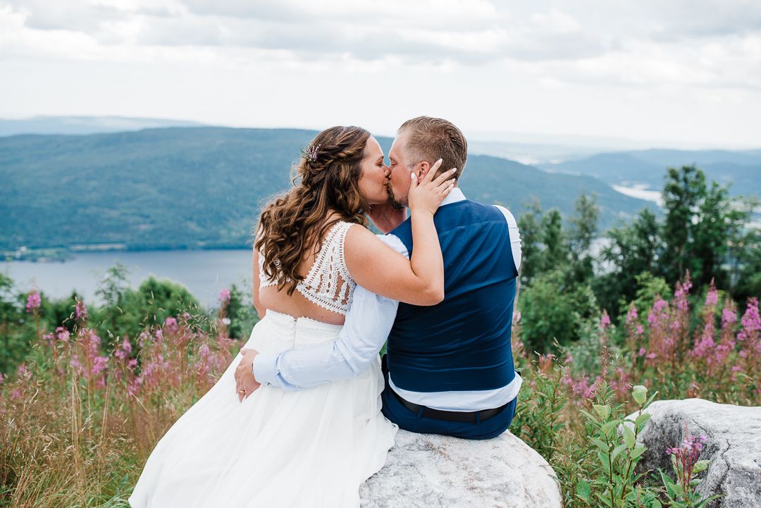 A romantic wedding moment with a couple sitting on a rock overlooking mountain vistas and flowering fields.
