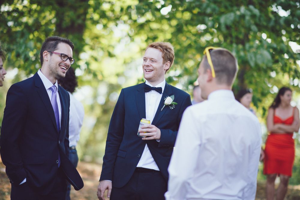 Wedding guests in formal attire chat during outdoor celebration under trees.