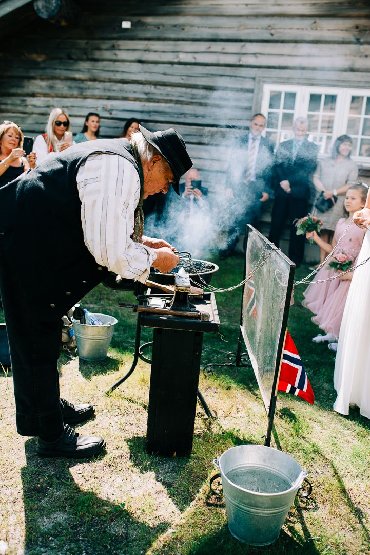 Blacksmith in period clothing works at outdoor forge during wedding celebration.