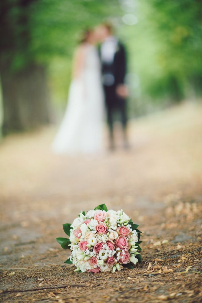 Wedding bouquet of pink and white flowers in foreground with blurred couple in background.
