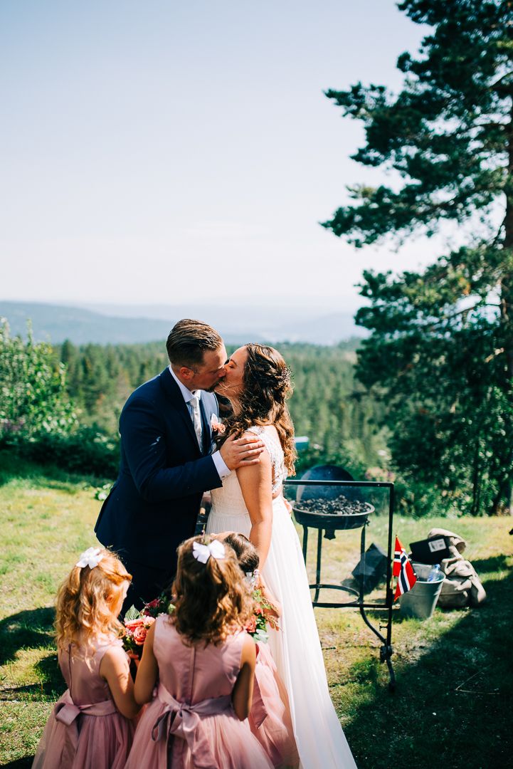 Romantic mountain wedding moment with attendants in pink dresses and scenic forest backdrop.