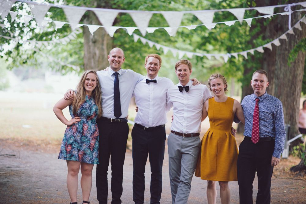 Group photo outdoors under white bunting decorations at a summer wedding celebration.