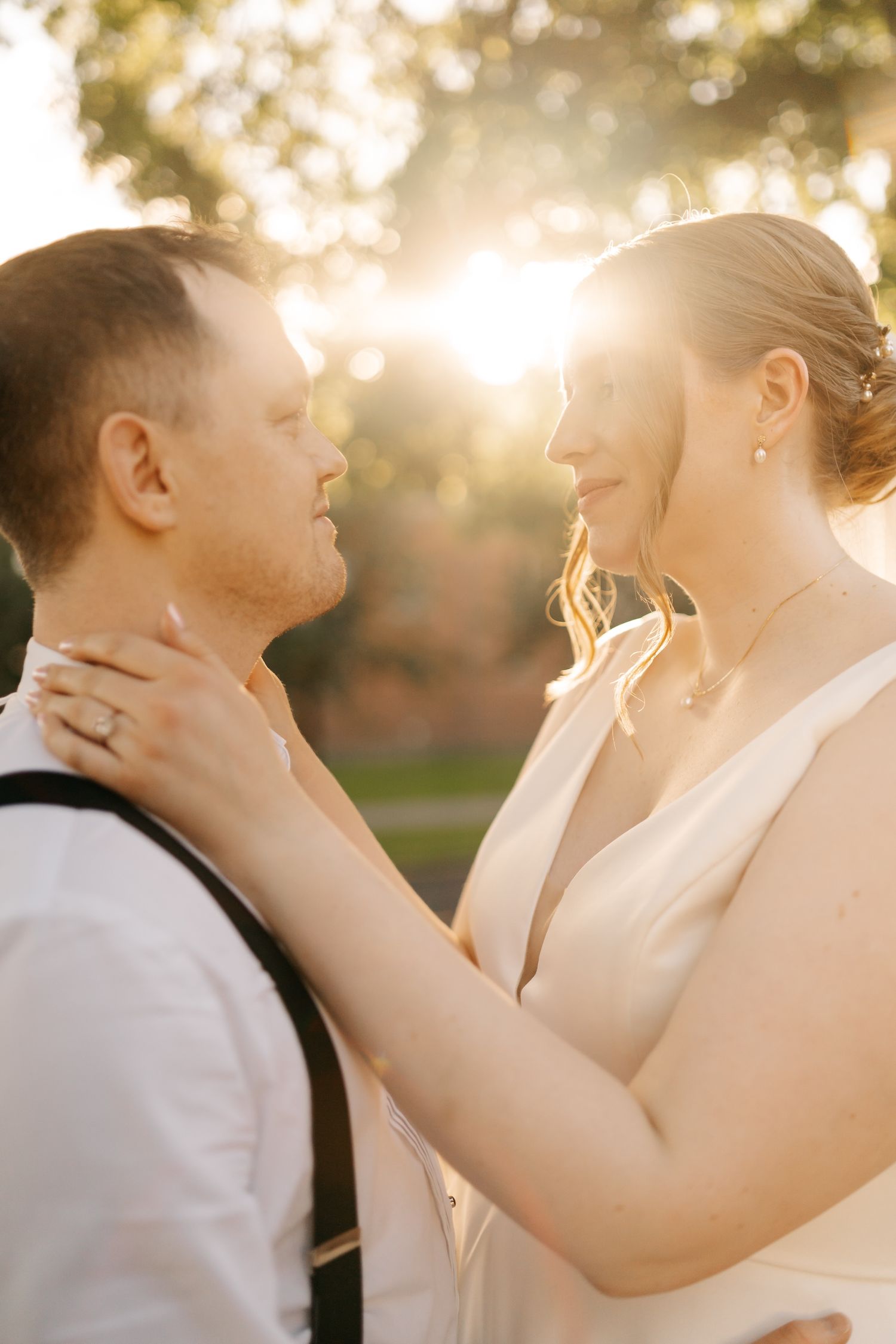 Bride and groom share an intimate moment outdoors, bathed in golden sunset light, with the bride in a white gown.