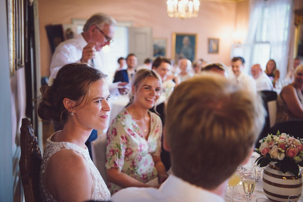 Wedding guests gather for indoor reception under chandelier lighting.