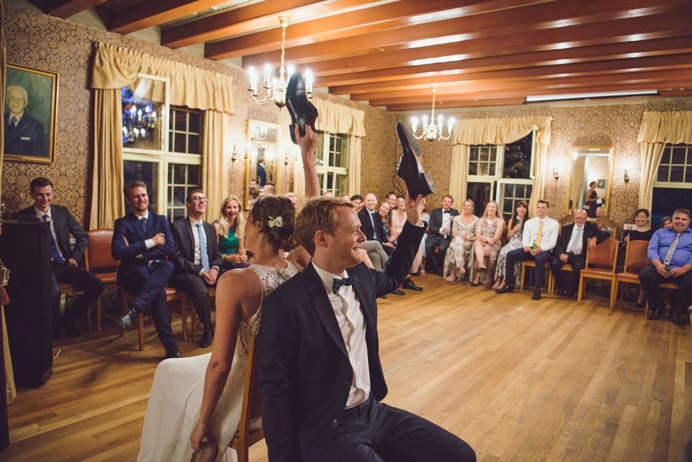 Reception guests in formal attire seated in a historic ballroom with wood beams and chandeliers.