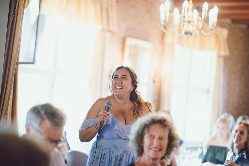 Wedding guest in lavender dress gives a toast during indoor reception.