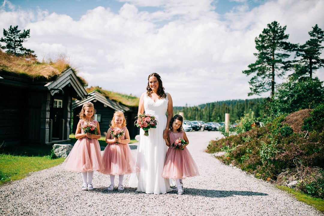 Wedding party walking along gravel path with traditional Norwegian cabin and pine trees in background.