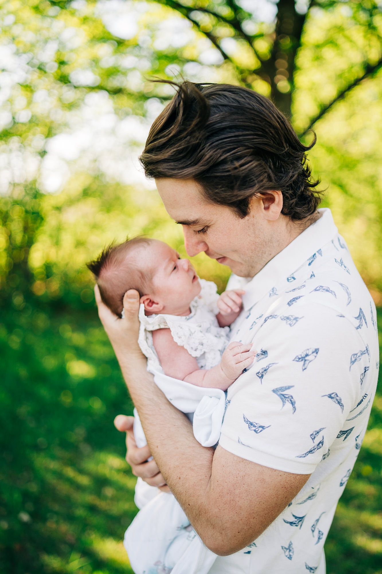 A tender moment shared between parent and newborn baby outdoors in a sunlit garden setting.